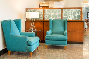 Un hall d’entrée avec deux fauteuils turquoise, une petite table avec une lampe et un comptoir d’accueil doté d’un panneau décoratif aux motifs géométriques.