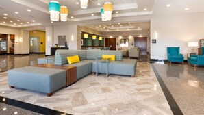 Eine geräumige Lobby mit einer Eckcouch, einem Couchtisch und sesseln in Türkis.