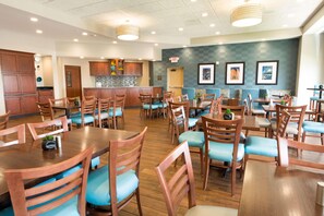 A spacious dining area with wooden tables and chairs, a kitchen in the background, and framed artwork on the walls. - Drury Inn Pikes Peak Colorado Springs (Colorado Springs)