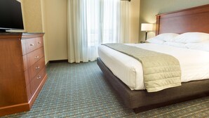 Una habitación de hotel con cama, cómoda, televisor y ventana con cortinas.