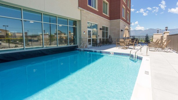 Una piscina con vistas a montañas, mobiliario exterior y un edificio con grandes ventanales.