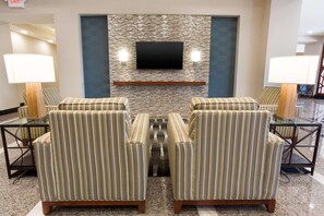 A lobby with striped armchairs, a flat-screen TV mounted on a textured wall, and two wall-mounted lamps. - Drury Inn Pikes Peak Colorado Springs (Colorado Springs)