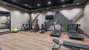 Un gimnasio con cintas de correr, elípticas y una máquina de remo.