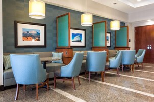 A hotel lobby with a seating area featuring blue chairs and a sofa, framed pictures on the wall, and a wooden door.
