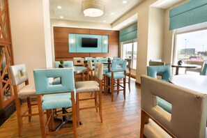 A hotel lobby with a wooden floor, light blue upholstered chairs, a flat-screen TV mounted on the wall, and large windows offering a view of the parking lot. - Drury Inn Pikes Peak Colorado Springs (Colorado Springs)