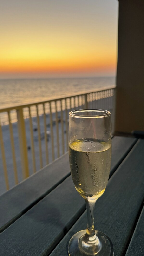 A glass of white wine on a wooden table with a view of the ocean and a sunset in the background. - Beachfront 3bedroom condo watch dolphins play from the balcony fitness room pool (Panama City Beach)
