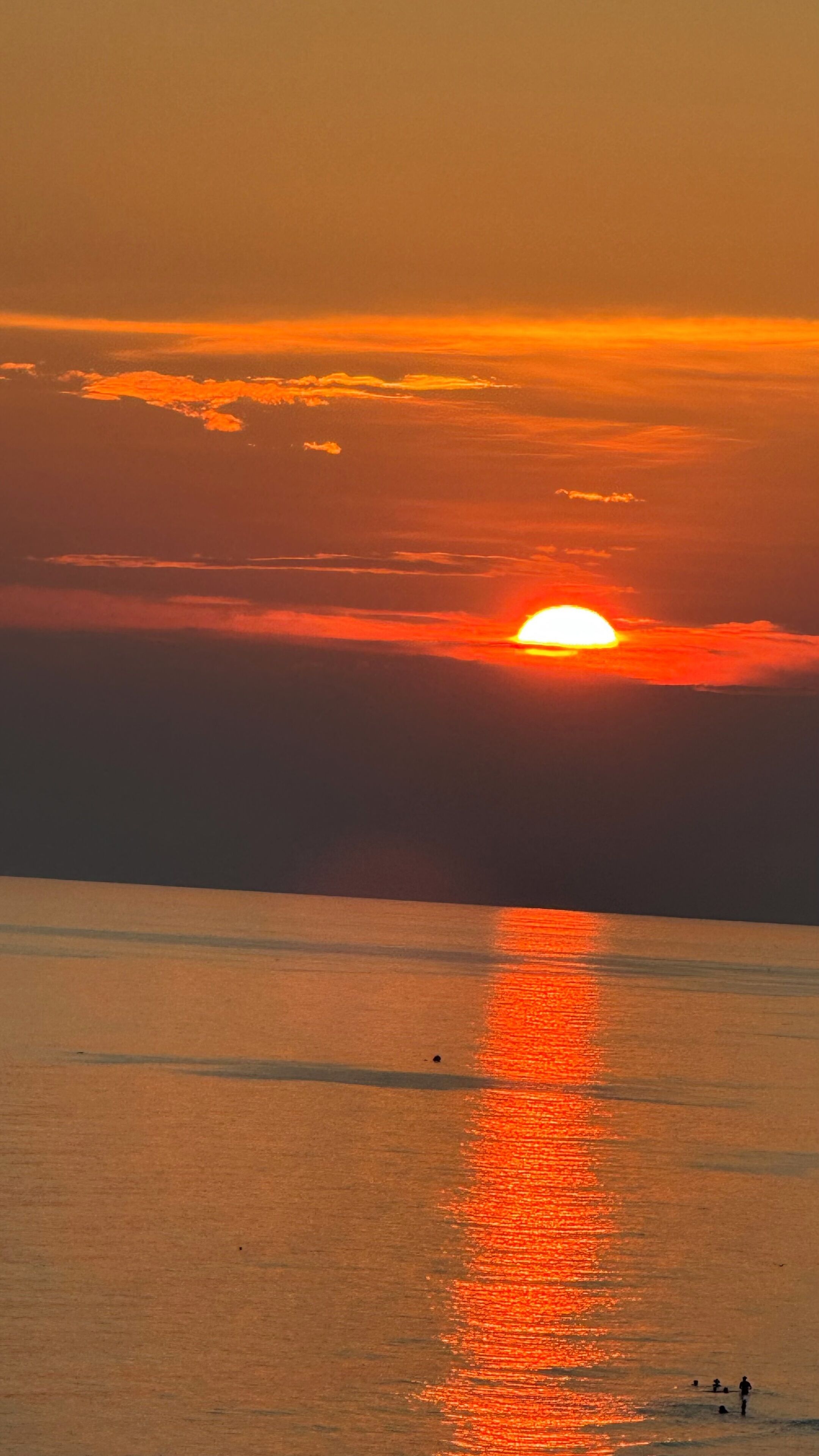 Un atardecer sobre un mar tranquilo con algunas personas en el agua.