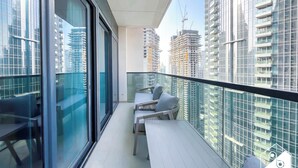 A balcony with a glass railing, a seating area with a table and chairs, and a view of high-rise buildings. - Skyline Elegance Fountain View 3BR in Downtown (Dubai)