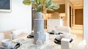 A modern living room with a marble coffee table, a large potted plant, and a dining area set for a meal. - Skyline Elegance Fountain View 3BR in Downtown (Dubai)