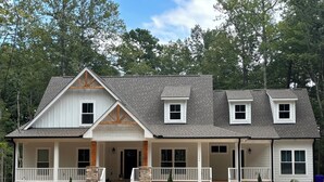 A two-story house with a front porch, a stone foundation, and a covered driveway.