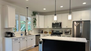 A modern kitchen with white cabinetry, stainless steel appliances, a central island, and pendant lighting.