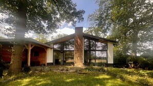 Una casa moderna con fachada de vidrio, chimenea de piedra y terraza de madera.