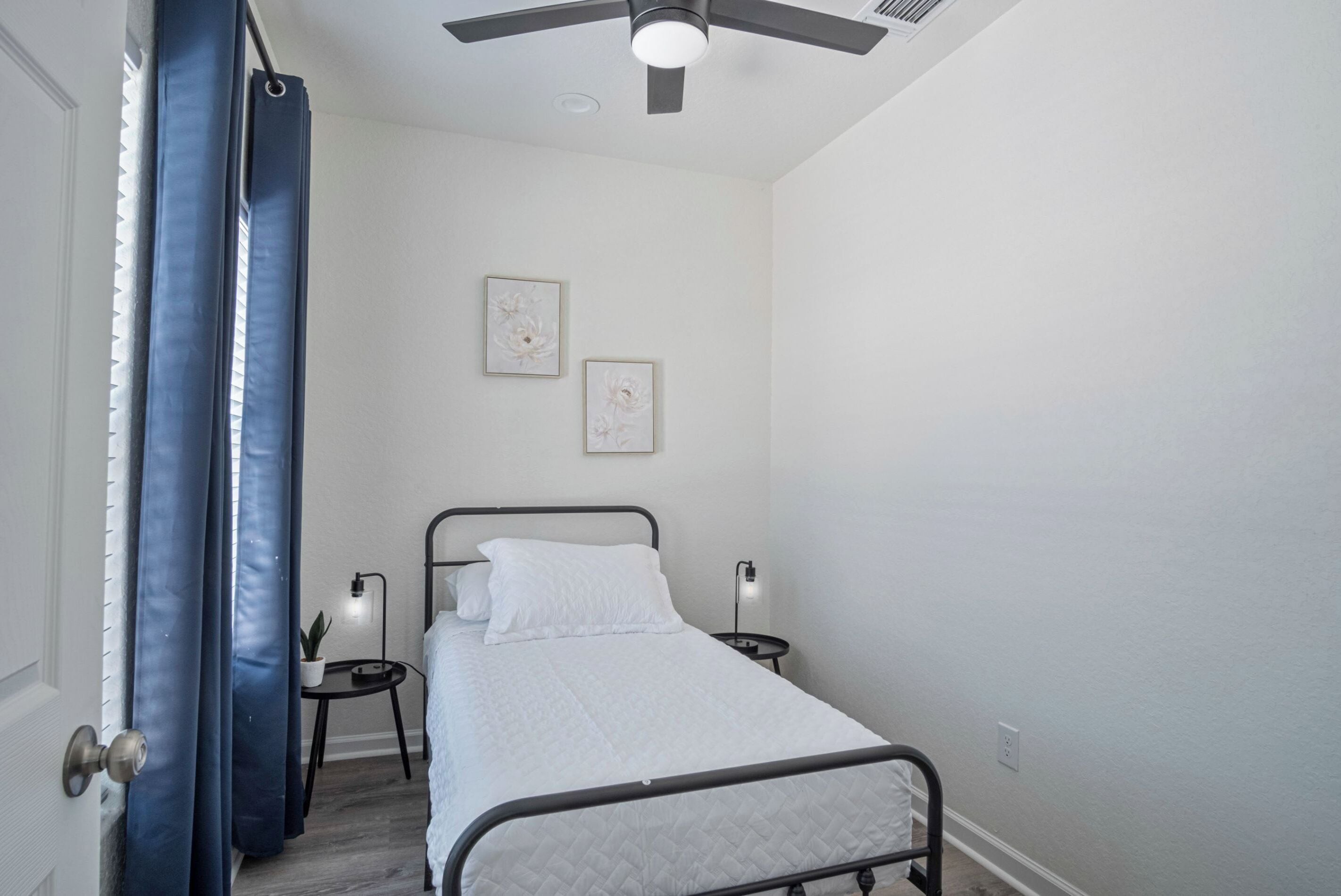 Un dormitorio con cama, dos luces en la pared, un ventilador de techo y una puerta con cortina.