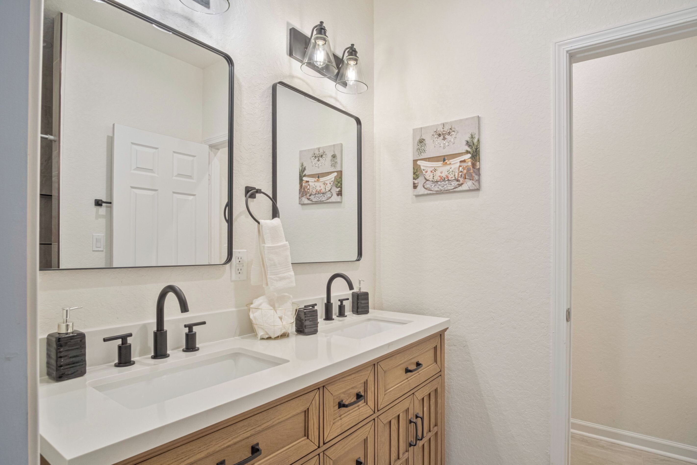 Une salle de bain dotée d’un meuble-lavabo à deux vasques, d’un meuble en bois, de deux miroirs fixés au mur et d’œuvres d’art décoratives murales.