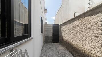 Un estrecho callejón con un sendero de grava, un muro de ladrillo a un lado y un edificio con un ventanal de marco negro al otro.