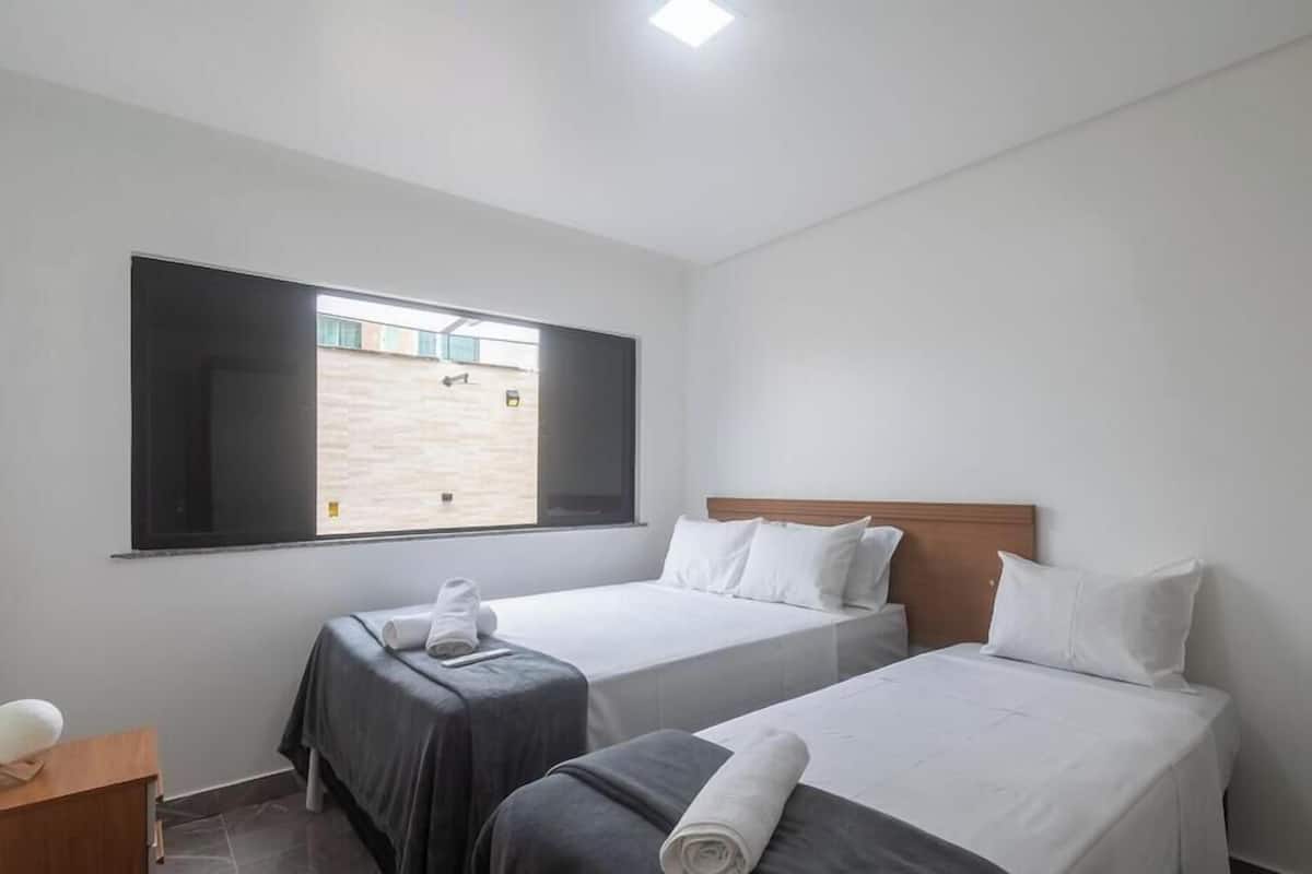 A hotel room with two single beds, a wooden headboard, a large window, and a small table with a lamp.