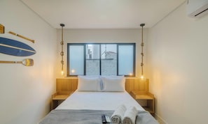 A bedroom with a bed, bedside tables, a window with a view, and a wall-mounted light fixture.