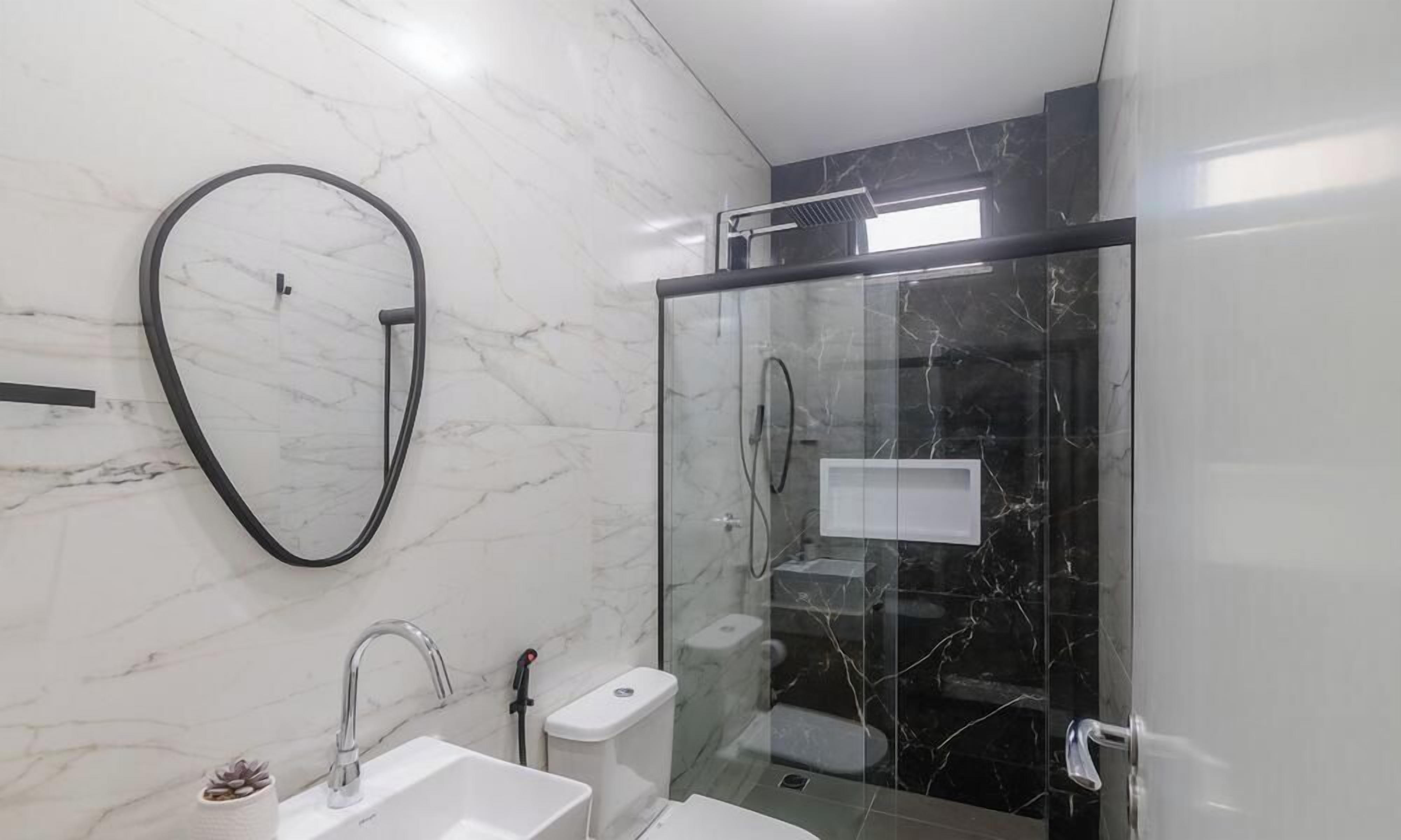 Un baño moderno con ducha envuelta en vidrio, un lavamanos blanco y una pared de mármol.
