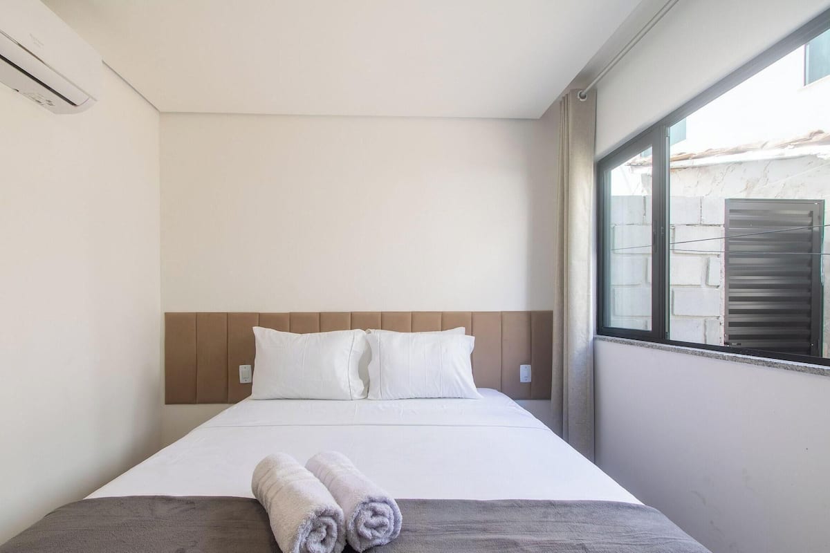 A single bed with a headboard, white bedding, and a window with a view of a building.