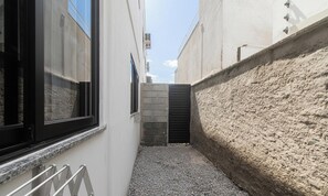 Une ruelle étroite avec un chemin de gravier, une porte noire et un bâtiment blanc doté d’une fenêtre.