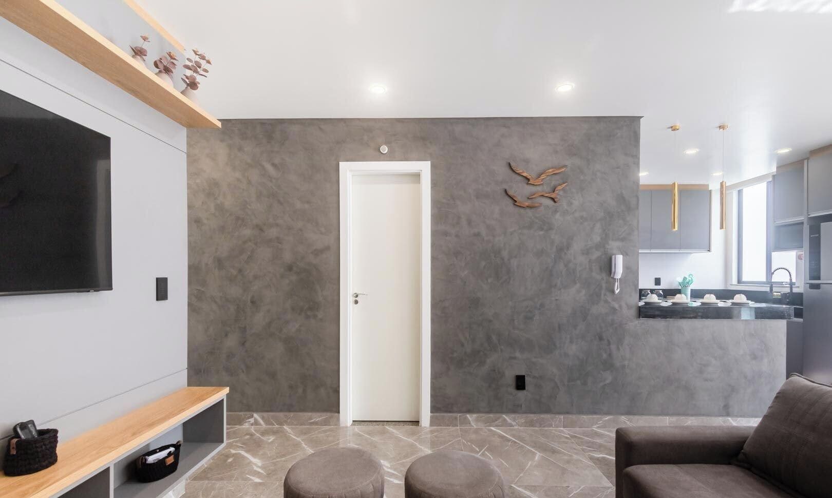 Un salon moderne avec un téléviseur à écran plat, une étagère en bois ornée d’objets décoratifs, un canapé gris et un sol en marbre.
