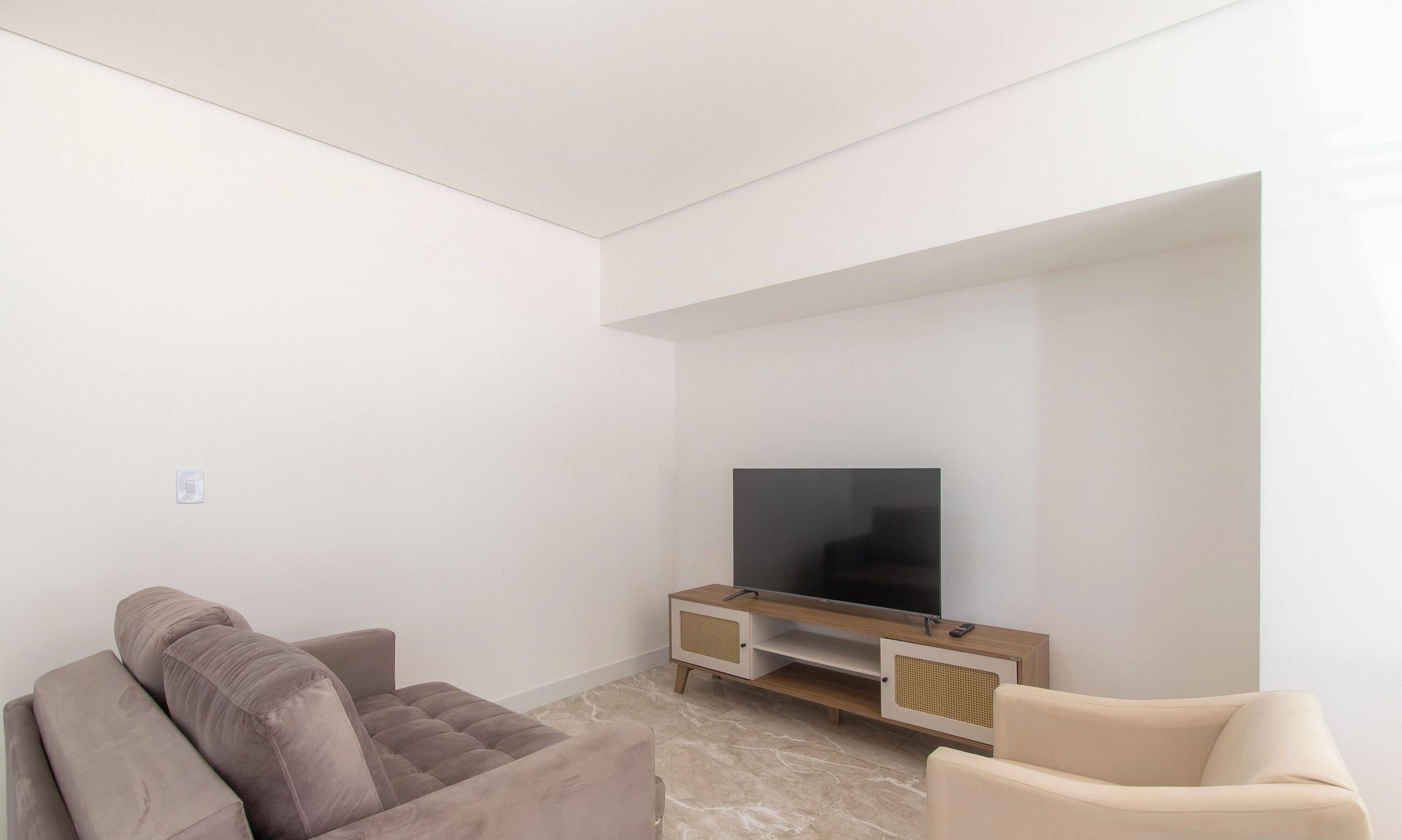 A minimalist living room with a flat-screen TV on a wooden stand, two sofas, and a light-colored floor.