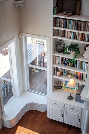A cozy reading nook with a built-in bench, a bookshelf filled with books, and a small table with a lamp. - Breakers Pointe by Ryson Vacation Rentals (Galveston)