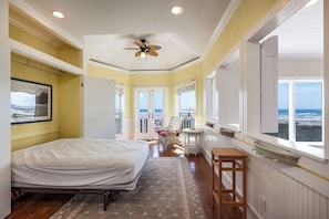 A bedroom with a bed, a ceiling fan, a window with a view of the ocean, and a door leading to another room. - Breakers Pointe by Ryson Vacation Rentals (Galveston)