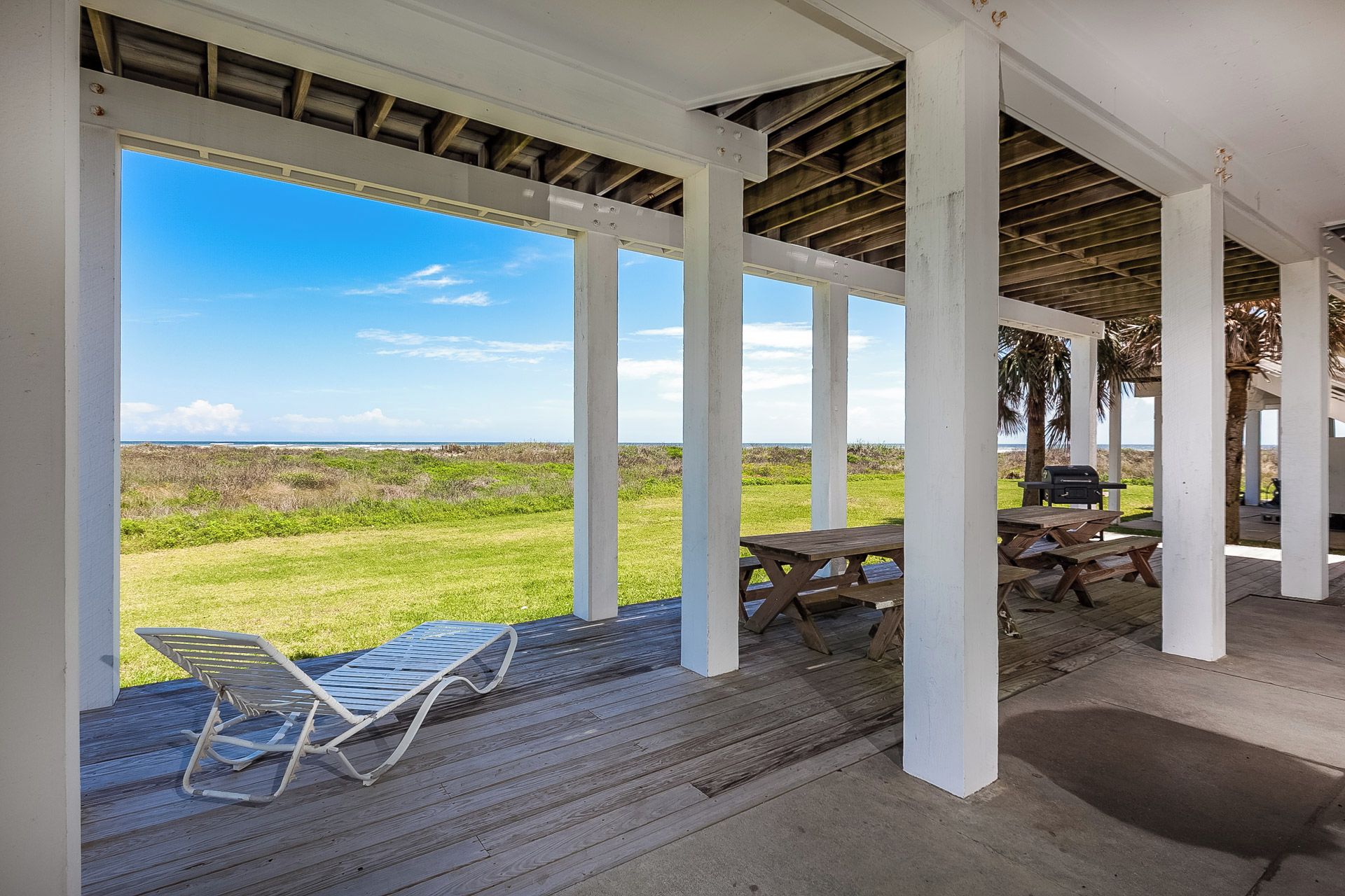 A covered outdoor area with a view of the ocean, wooden deck, and picnic tables.