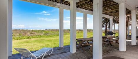 A covered outdoor area with a view of the ocean, wooden deck, and picnic tables.