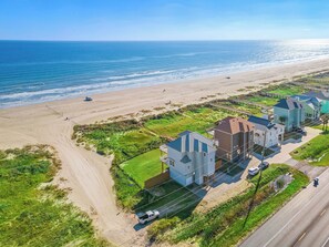 An aerial view of a coastal residential area with houses, a beach, and a road. - Beach Heaven by Ryson Vacation Rentals (Galveston)