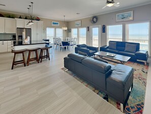 A modern living room with a gray sofa, a coffee table, and a dining area with white chairs. - Beach Heaven by Ryson Vacation Rentals (Galveston)