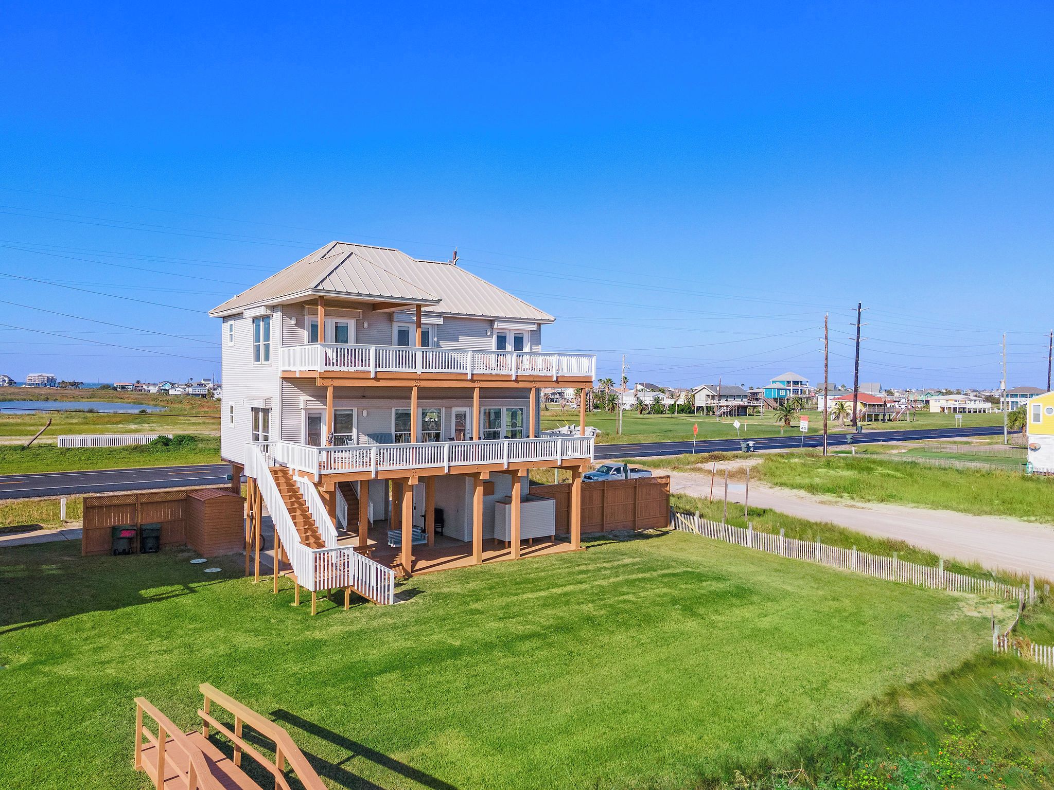 A two-story building with a balcony and a covered area, surrounded by a grassy area and a road.