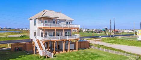 A two-story building with a balcony and a covered area, surrounded by a grassy area and a road.