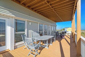 A covered outdoor deck with a wooden ceiling, white railings, and a table with chairs. - Beach Heaven by Ryson Vacation Rentals (Galveston)