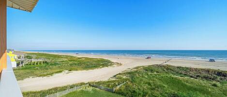A beach view from a balcony with a wooden railing, a sandy path, and a wooden fence.