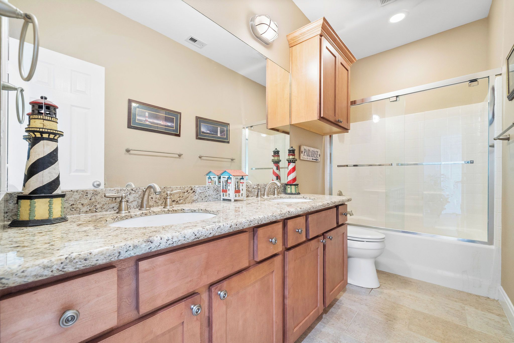 A bathroom with a granite countertop, wooden cabinets, a white toilet, and a glass-enclosed shower.