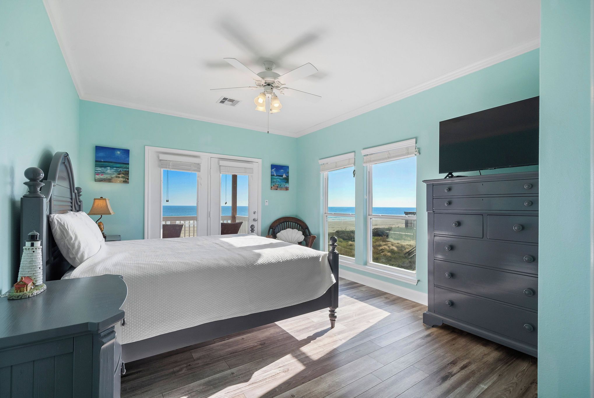 A bedroom with a bed, dresser, and a TV on a dresser. There are two windows and a ceiling fan.