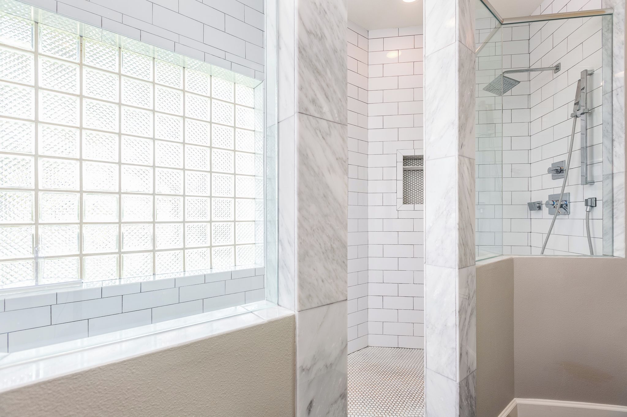 Un baño moderno con azulejos de mármol blanco, cabina de ducha de vidrio y un ventanal con diseño de cuadrícula.