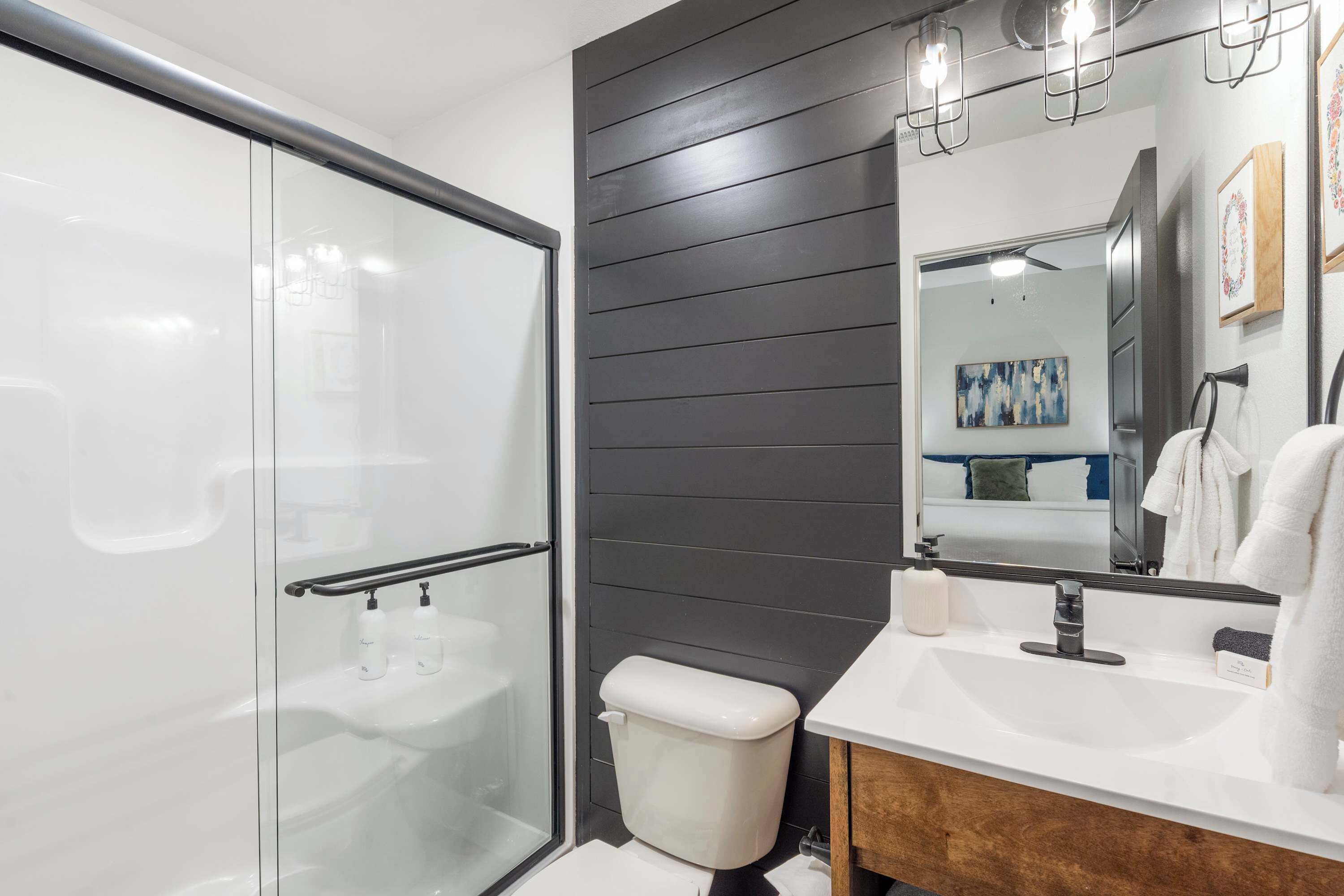 Een moderne badkamer met een glazen douchecabine, een witte wastafel en een wandpaneel van donker hout.