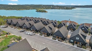 A row of dark-roofed cabins with a parking lot in front, overlooking a large body of water and a small island.