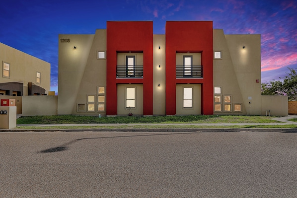 A modern building with two red sections and beige walls, featuring balconies and large windows.