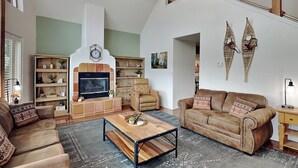 A spacious living room with a fireplace, leather sofas, a coffee table, and a bookshelf.