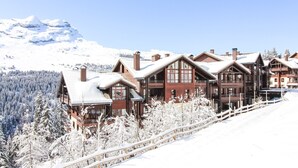 Un chalet enneigé composé de plusieurs bâtiments, une clôture en bois et, en arrière-plan, une montagne couverte de neige.
