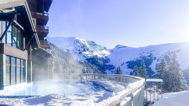 Un paysage montagneux enneigé, avec un bâtiment doté de grandes fenêtres et d’une partie entièrement vitrée.