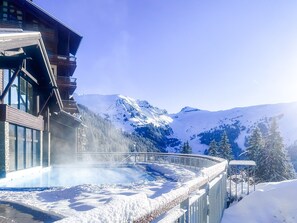 Un paysage montagneux enneigé, avec un bâtiment doté de grandes fenêtres et d’une partie entièrement vitrée.