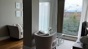 Ein modernes Wohnzimmer mit großem Fenster, einer Couch, einem Sessel und einem kleinen Tisch mit einer Vase.