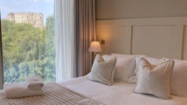 Ein Hotelzimmer mit einem großen Bett, Blick auf ein Schloss durch das Fenster und einer Lampe auf dem Nachttisch.