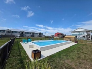 A swimming pool with a fenced area, a small trash bin, and a grassy lawn.
