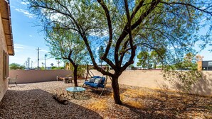 A patio area with a table and chairs, a swing, and a tree.